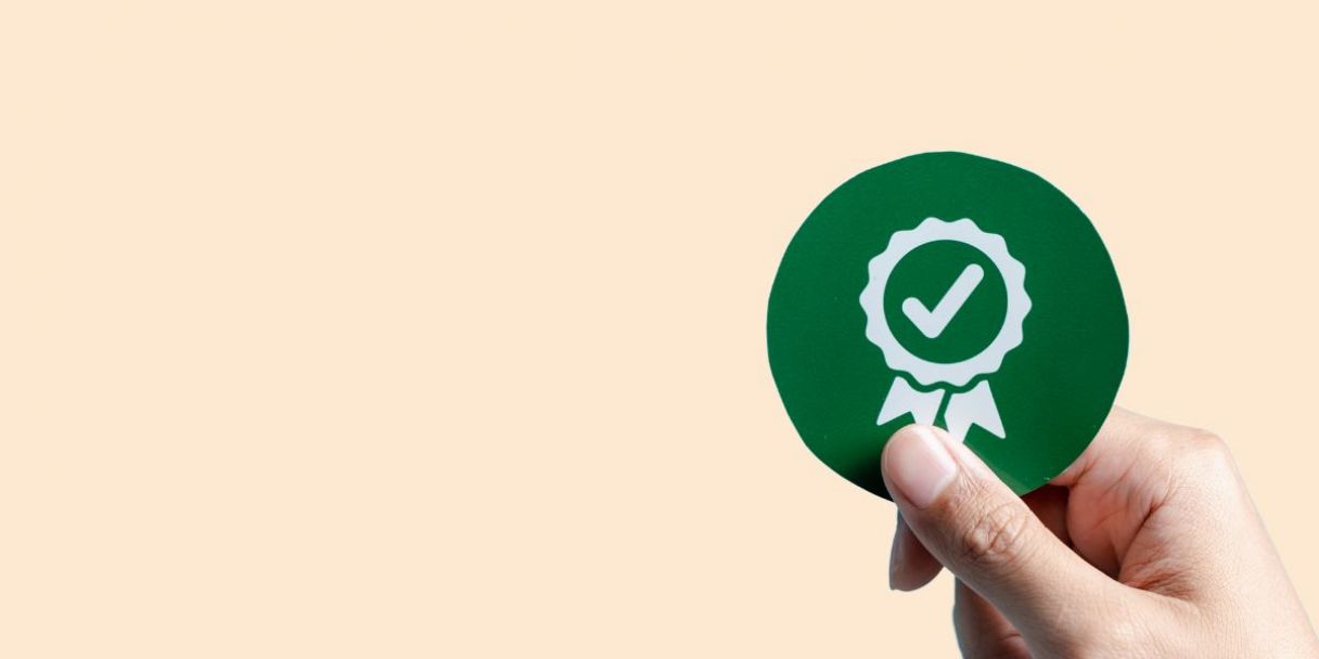 a hand holding up a compliance check badge
