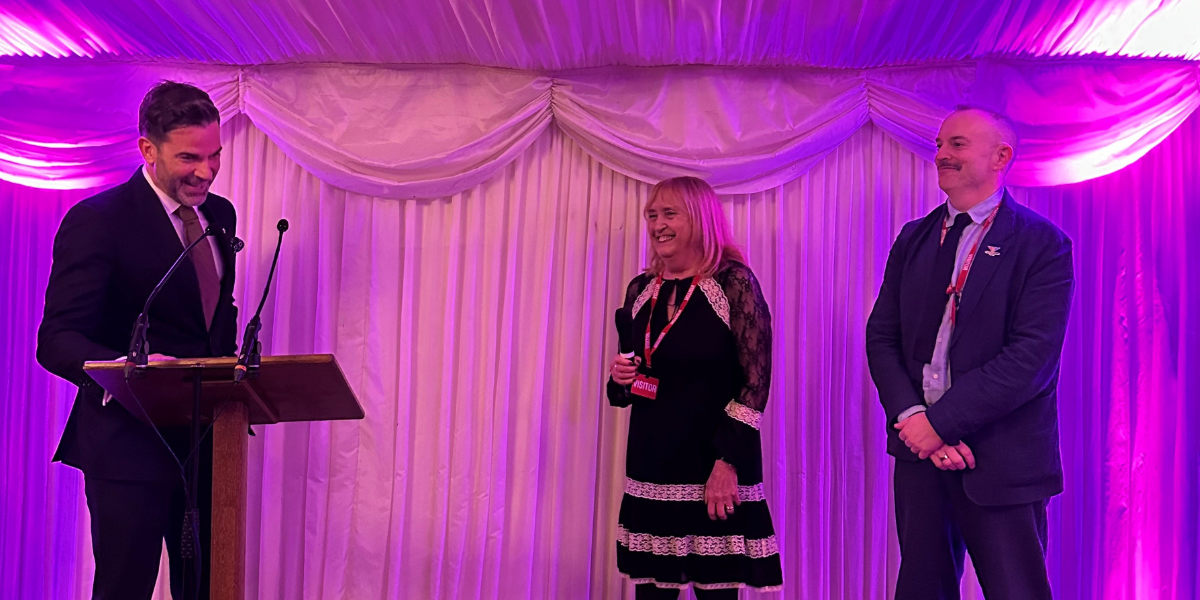mauve group ceo ann ellis and commonwealth sport deputy ceo martin reynolds standing on a stage lit by purple lighting