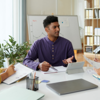 Three Indians sitting at a table, discussing documents and using a tablet in a modern office setting