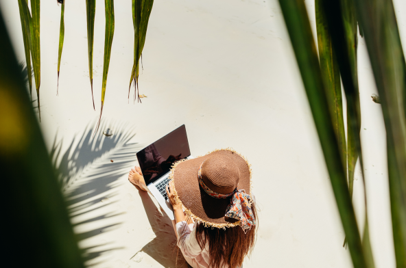 A digital nomad worker on a beach, wearing a sun hat